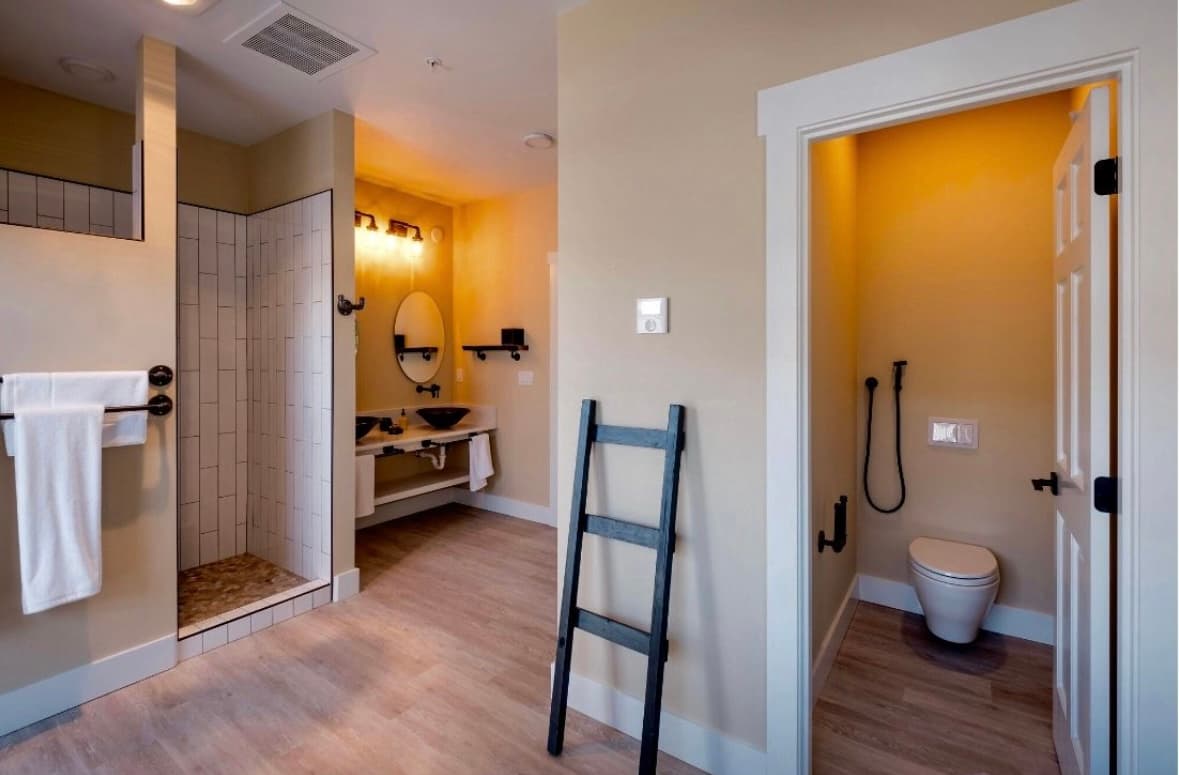 A modern bathroom featuring a shower, sink, and toilet with warm beige walls and wooden accents.